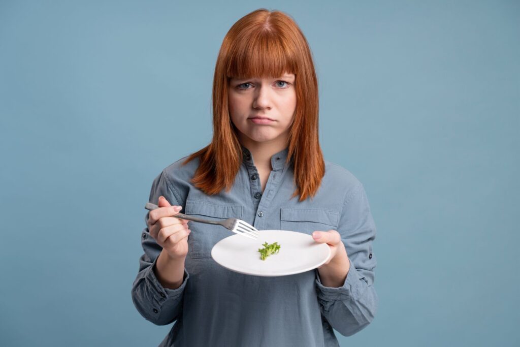Disgruntled woman holding a plate with small porrtion food on it, Weight Loss Myths Debunked